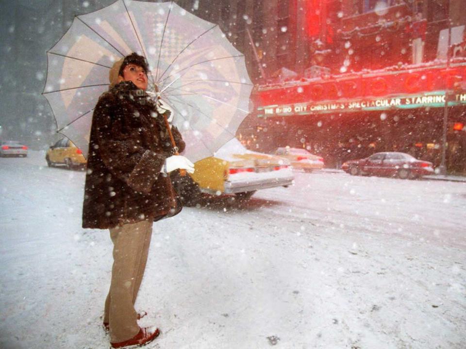 A woman looks skyward as she waits to cross the street outside Radio City Music Hall during the heavy snowfall 07 January in New York. A blizzard which is working its way up the east coast of the United States is expected to dump up to two feet of snow in New York City.