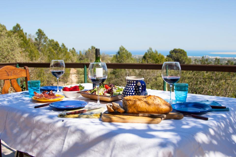 A table overlooking the ocean, featuring a loaf of bread, a big salad, and several glasses of wine.