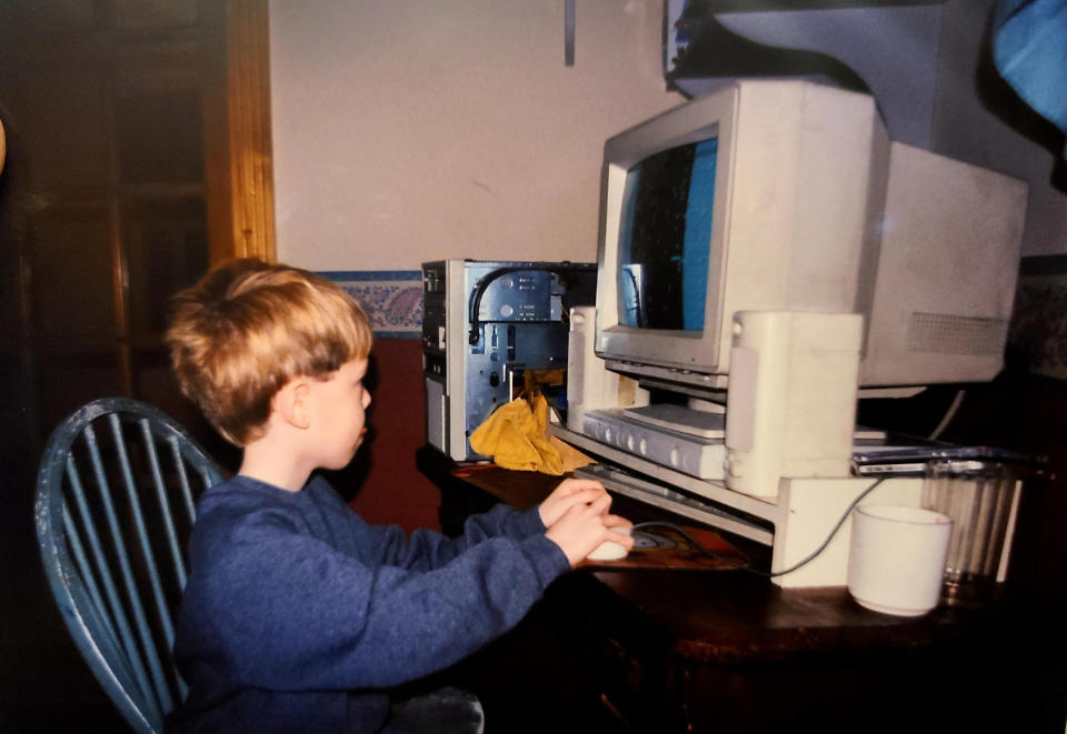 Young boy using an old desktop computer with a CRT monitor, mouse, and keyboard. An open computer tower is on the desk beside him