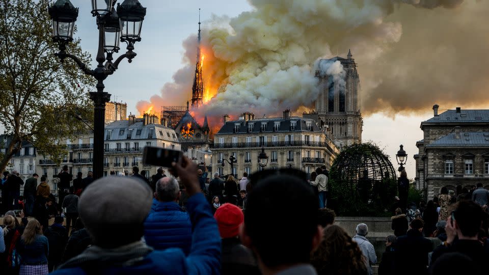 People watch the landmark Notre-Dame cathedral burning in central Paris on April 15, 2019- Investigations did not identify the exact cause of the fire. - Nicolas Liponne/NurPhoto/Getty Images