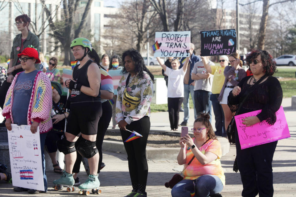 Some of the more than 100 participants listen to speakers at rally outside the Kansas Statehouse on Transgender Day of Visibility, Friday, March 31, 2023, in Topeka, Kan. Republican lawmakers in Kansas and other states are pursuing several hundred proposals that would roll back transgender rights, including measures to ban transgender athletes from girls' and women's sports and to prohibit gender-affirming medical care for minors. (AP Photo/John Hanna)