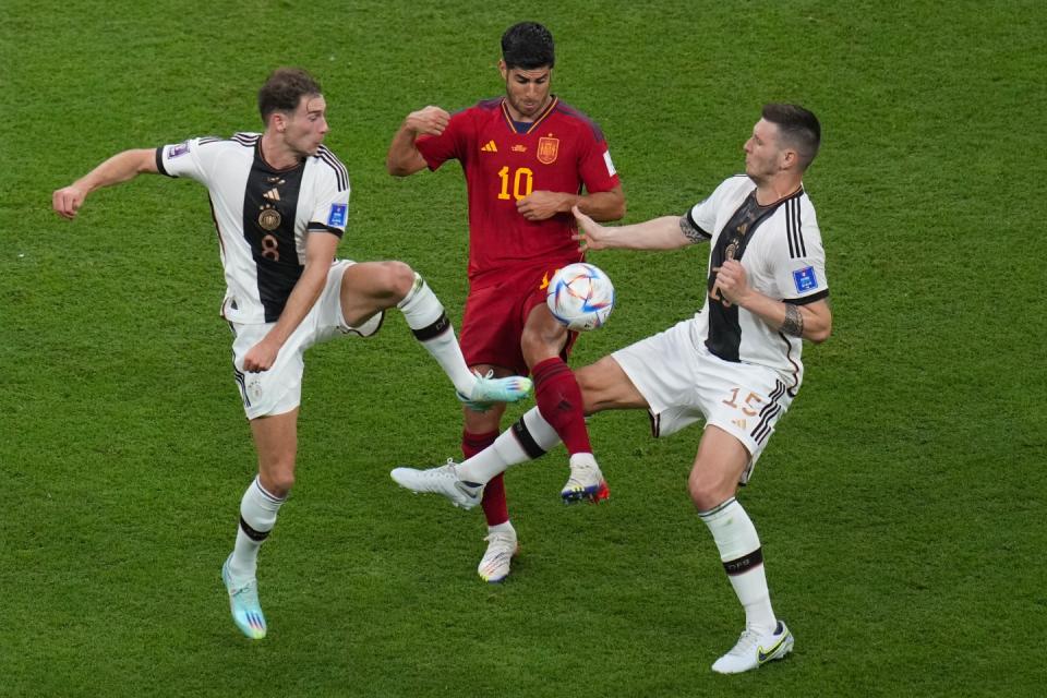 Spain's Marcos Asensio, centre, challenges for the ball with Germany's Leon Gorentzka, left, and Germany's Niklas Suele during the World Cup group E football match between Spain and Germany, at the Al Bayt Stadium in Al Khor, Qatar, Sunday, Nov. 27, 2022. (AP Photo/Ricardo Mazalan)