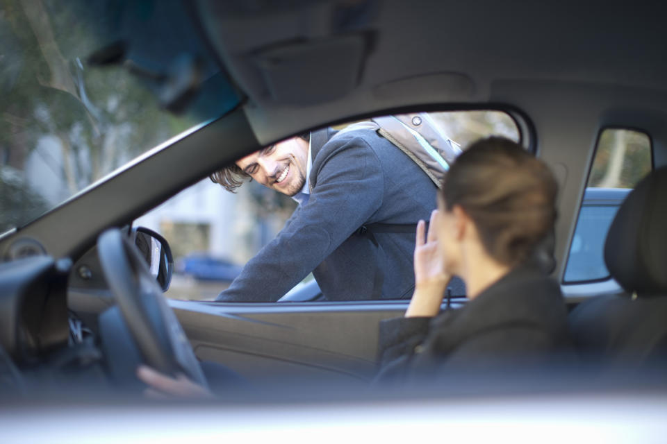 Young businesswoman driving and waving at male cyclist.