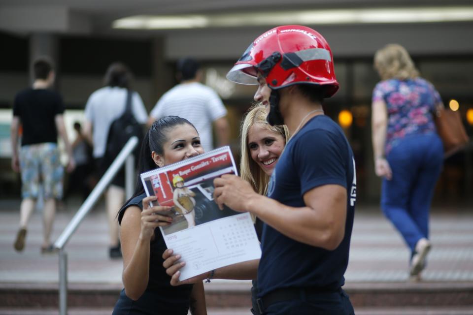 In this Jan. 13, 2019 photo, firefighter Daniel Rodriguez sells calendars to a couple of women in Asuncion, Paraguay. Firefighters in the town of San Roque Gonzalez launched a campaign to sell calendars featuring nude pictures of themselves, to help fund their fire station. (AP Photo/Jorge Saenz)
