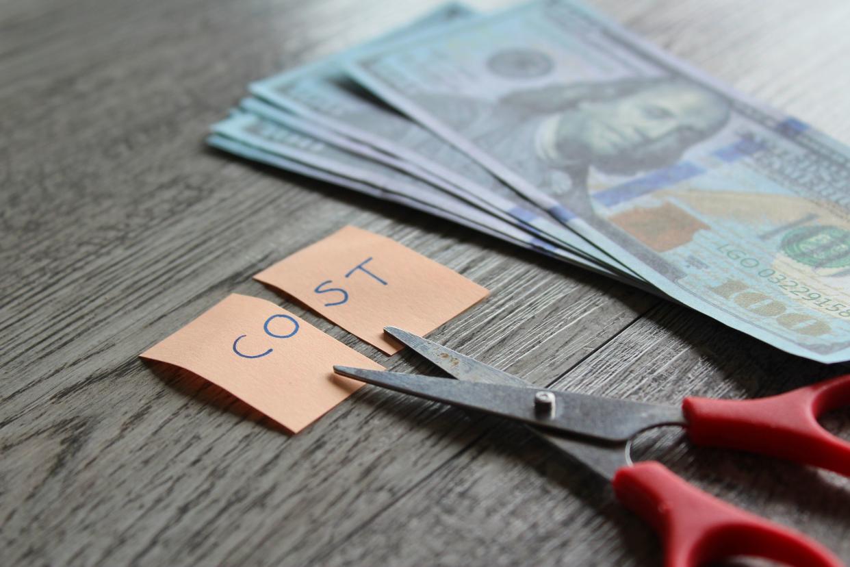 Scissor, money and note with text COST. Financial, cost cutting, reduce expenses concept