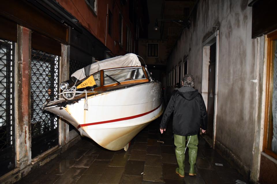 A man looks at a stranded taxi boat lying on its side in a alley in Venice, early Wednesday, Nov. 13, 2019. The mayor of Venice is blaming climate change for flooding in the historic canal city that has reached the second-highest levels ever recorded, as another exceptional water level was recorded Wednesday. The high-water mark hit 187 centimeters (74 inches) late Tuesday, meaning more than 85% of the city was flooded. (AP Photo/Luigi Costantini)