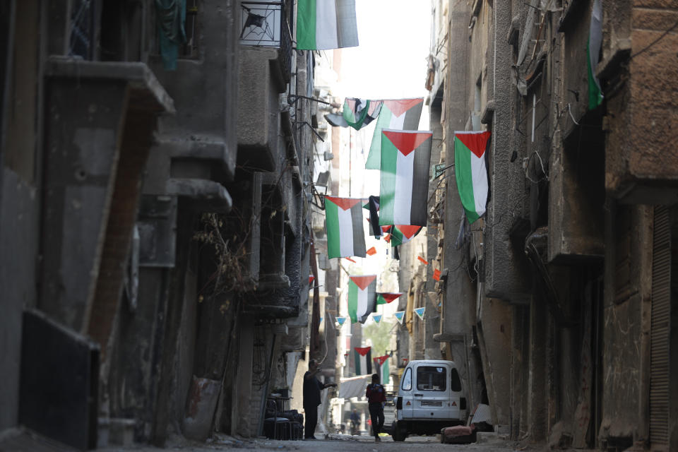 File - People walk under Palestinian flags in Yarmouk camp in Damascus Syria that has seen heavy fighting during the civil war, Wednesday, Nov. 2, 2022. A trickle of residents has returned to Yarmouk, the large Palestinian refugee camp-turned-Damascus neighborhood that was devastated in the country's civil war. (AP Photo/Omar Sanadiki, File)