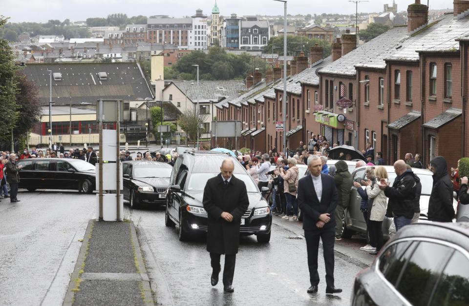 The funeral cortege of the former Northern Ireland lawmaker and Nobel Peace Prize winner John Hume passes through the streets as people bow their heads following the funeral Mass at St Eugene's Cathedral in Londonderry, Northern Ireland, Wednesday, Aug. 5, 2020. Hume was co-recipient of the 1998 Nobel Peace Prize with fellow Northern Ireland lawmaker David Trimble, for his work in the Peace Process in Northern Ireland. Masks are worn due to the ongoing Coronavirus outbreak . (AP Photo/Peter Morrison)