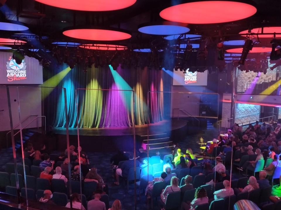 A cruise ship auditorium filled with people and colorful lights.