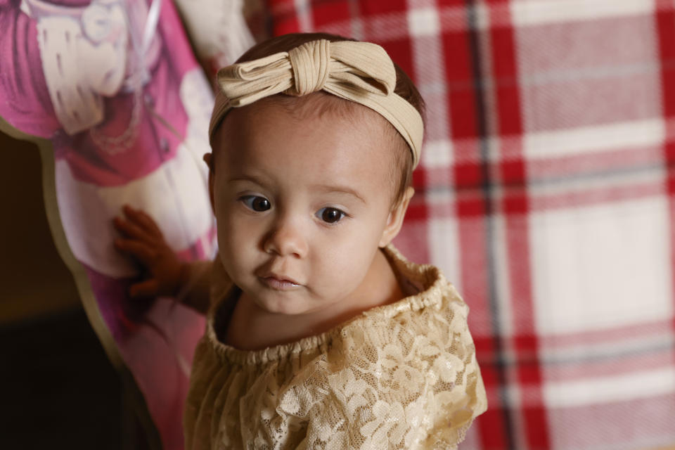 One-year-old Cora Dibert stands in The Bridge Church, Saturday, Dec. 2, 2023, in Mustang, Okla. Cora is among dozens of young kids across the U.S. poisoned by lead linked to tainted pouches of the cinnamon-and-fruit puree. (AP Photo/Nate Billings)