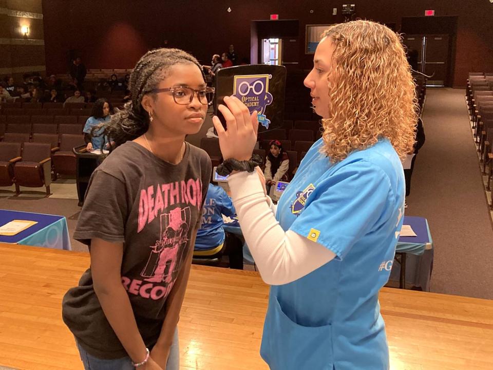 Roblei Mustaf, 13, tries on eyeglass frames as Ashly Espiritusanto, event coordinator for Optical Academy, holds a mirror during a Glasses2Classes free eyeglass event Feb. 20 at East Middle School.