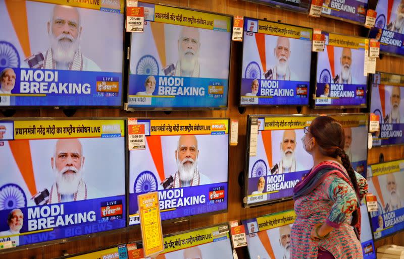 A woman wearing a protective mask watches Indian PM Modi on TV screens inside a showroom in Ahmedabad