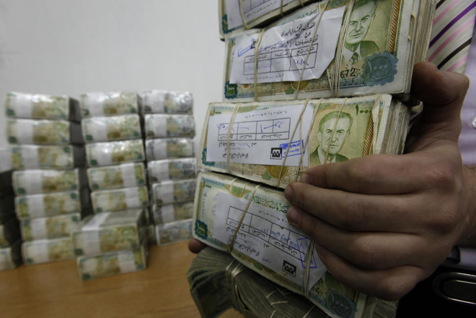 FILE - In this January 13, 2010 file photo, a Syrian employee, holds packets of Syrian currency in the Central Syrian Bank in, Damascus, Syria. With Syria's currency hitting record lows, a nationwide symbolic campaign has been launched by merchants, barbers, supermarkets and even gyms to support the Syrian pound. (AP Photo/Hussein Malla, File)