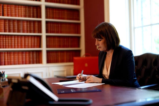 Chancellor Rachel Reeves sits at her desk in the Treasury, with a pen in hand and pieces of paper on the desk in front of her. Her red ministerial box sits in the background.