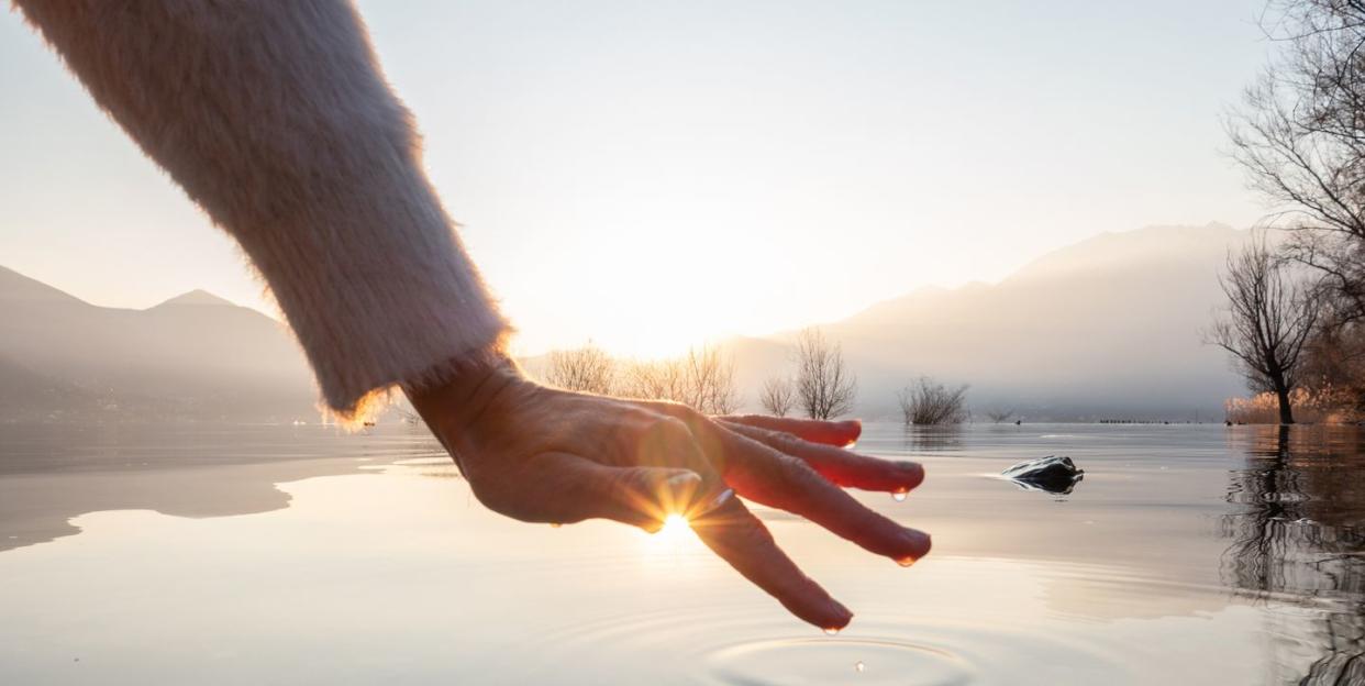 detail of hand touching water surface of lake at sunset