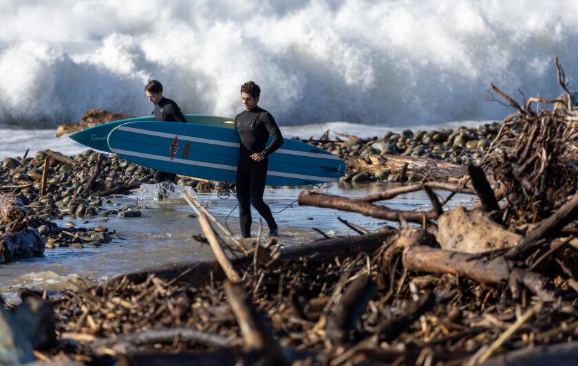 Ventura, CA - December 28: Surfers navigate rocks and driftwood at Surfer's Point as they look for a spot to enter the water as large waves pound the beach on Thursday, Dec. 28, 2023 in Ventura, CA. (Brian van der Brug / Los Angeles Times)