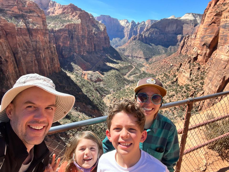 A family of four posing next to a railing next to a dramatic view of Zion National Park