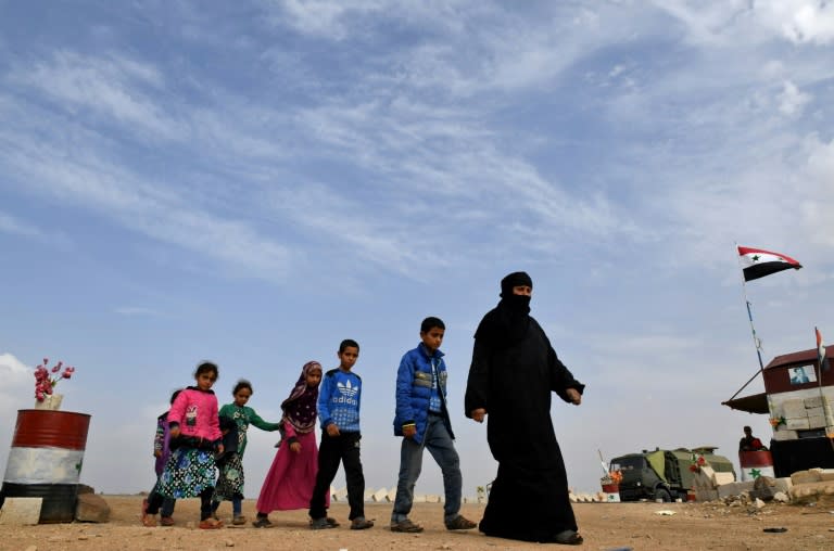 Syrian families walk as members of Russian and Syrian forces stand guard at the Abu Duhur crossing on the eastern edge of Syria's Idlib province on October 23, 2018.Civilians are coming from rebel-held areas in Idlib province and entering regime-held territories through the Abu Duhur crossing, some of them returning to their villages that were recaptured by the regime forces earlier this year