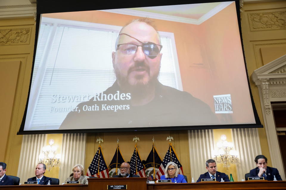Oath Keepers founder Stewart Rhodes, with eye patch, is seen on video at a hearing, above the seated members of the House panel.