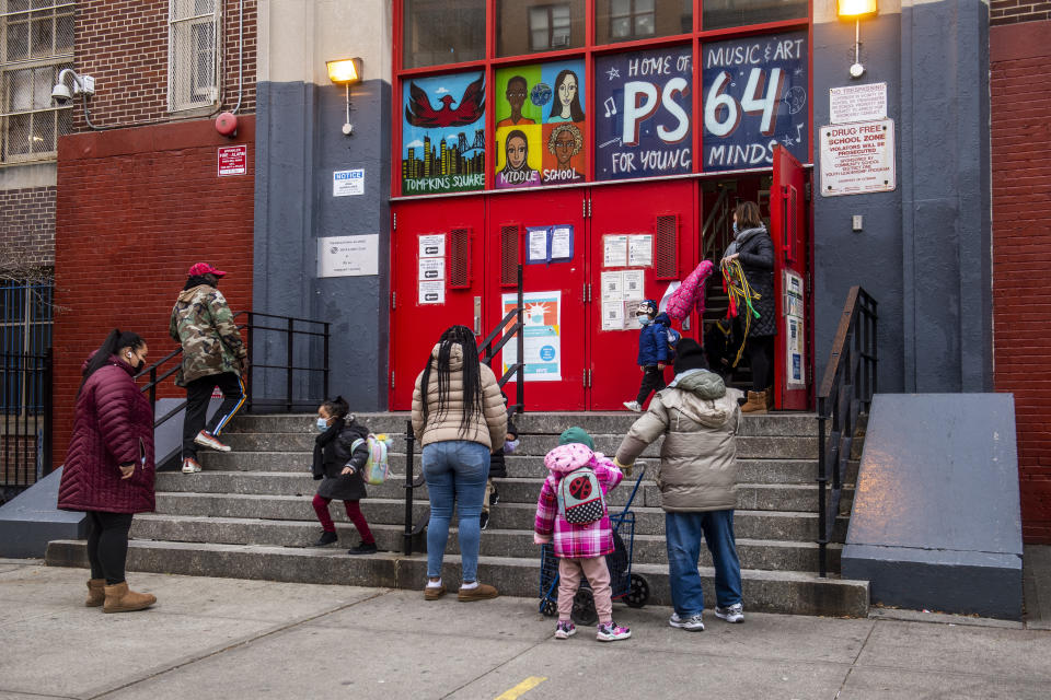 Parents pick up their children while wearing masks outside of P.S. 64 in the East Village neighborhood of Manhattan, Tuesday, Dec. 21, 2021, in New York. (AP Photo/Brittainy Newman)