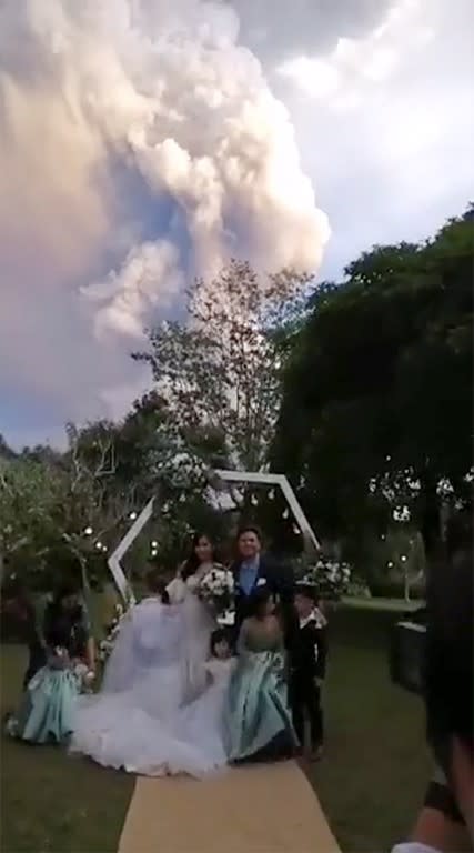 A couple poses during their wedding ceremony as Taal Volcano sends out a column of ash in the background, in Alfonso