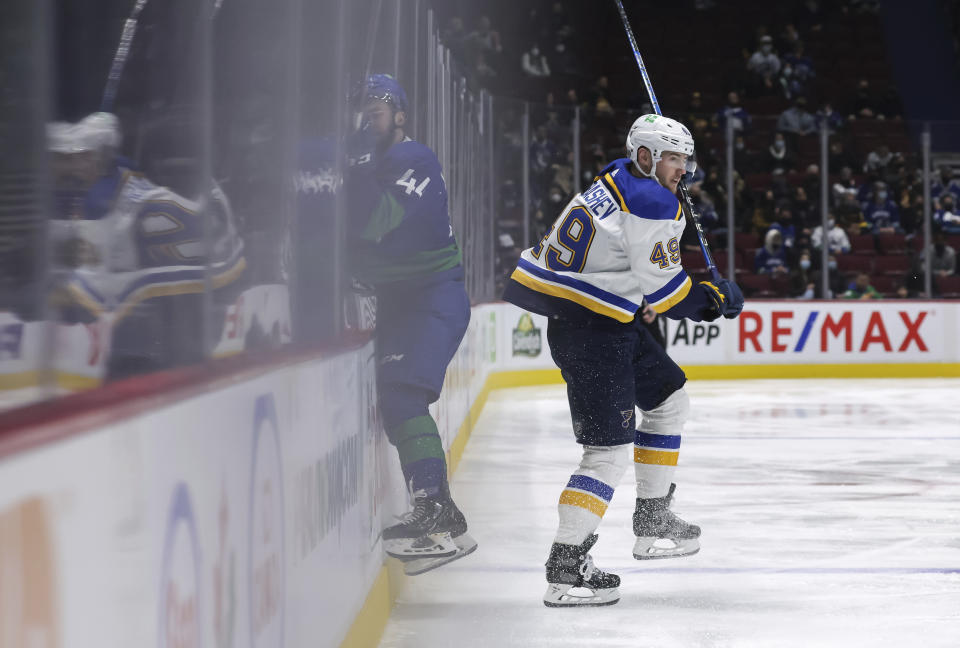 Vancouver Canucks' Kyle Burroughs, left, misses the check on St. Louis Blues' Ivan Barbashev, of Russia, and crashes into the boards during the third period of an NHL hockey game in Vancouver, British Columbia, Sunday, Jan. 23, 2022. (Darryl Dyck/The Canadian Press via AP)