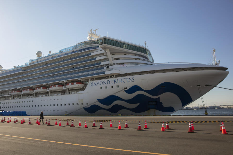 A reporter walks near the quarantined Diamond Princess cruise ship in Yokohama, near Tokyo, Tuesday, Feb. 11, 2020. Japan's Health Minister Katsunobu Kato said the government was considering testing everyone remaining on board and crew on the Diamond Princess, which would require them to remain aboard until results were available. (AP Photo/Jae C. Hong)