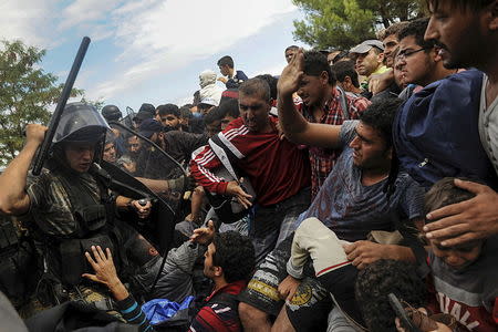 A Macedonian police officer raises his baton towards migrants to stop them from entering into Macedonia at Greece's border near the village of Idomeni, Greece, August 22, 2015. REUTERS/Alexandros Avramidis