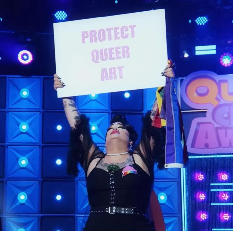 Megami holding up a protect queer art sign