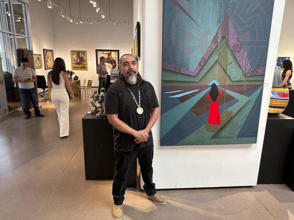 Artist Thomas "Breeze" Marcus attends an exhibition opening of his work at Blue Rain Gallery in Santa Fe, N.M. on Thursday, Aug. 17, 2023, including the painting titled "Answered Prayer," background. A separate group exhibition that included his work was postponed in Arizona amid outrage over a painting by Shepard Fairey that is critical of police. It's the latest of several recent incidents around the U.S. where artists in public spaces have had the rug pulled out from under them because of the content of their work. (AP Photo/Morgan Lee)