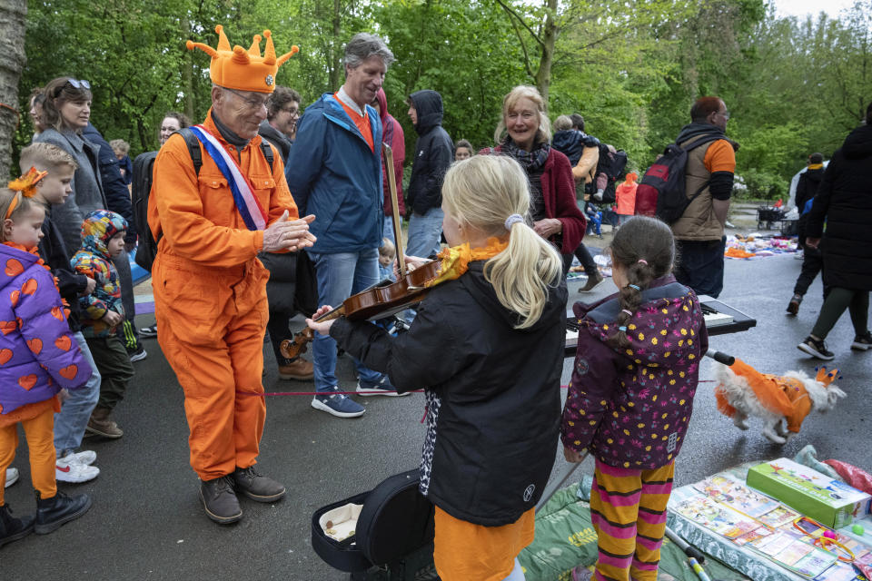 An orange-clad man applauds for a girl playing violin as his orange-clad dog, bottom right corner, runs off during King's Day celebrations in Amsterdam, Netherlands, Saturday, April 27, 2024. (AP Photo/Peter Dejong)