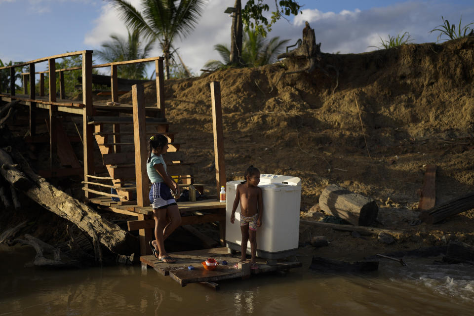 Amerindian children wait for a washing machine to complete its cycle, on the banks of the Barama River in Chinese Landing, Guyana, Monday, April 17, 2023. Called Chinese Landing for reasons residents no longer remember, the village is deep within lush forests of northern Guyana accessible primarily by riverboat. (AP Photo/Matias Delacroix)