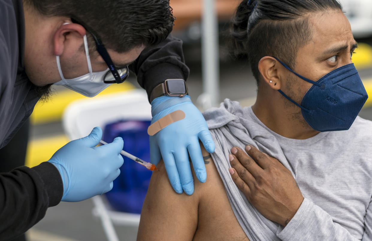 A man wearing protective gloves injects a vaccine into another man’s arm. 