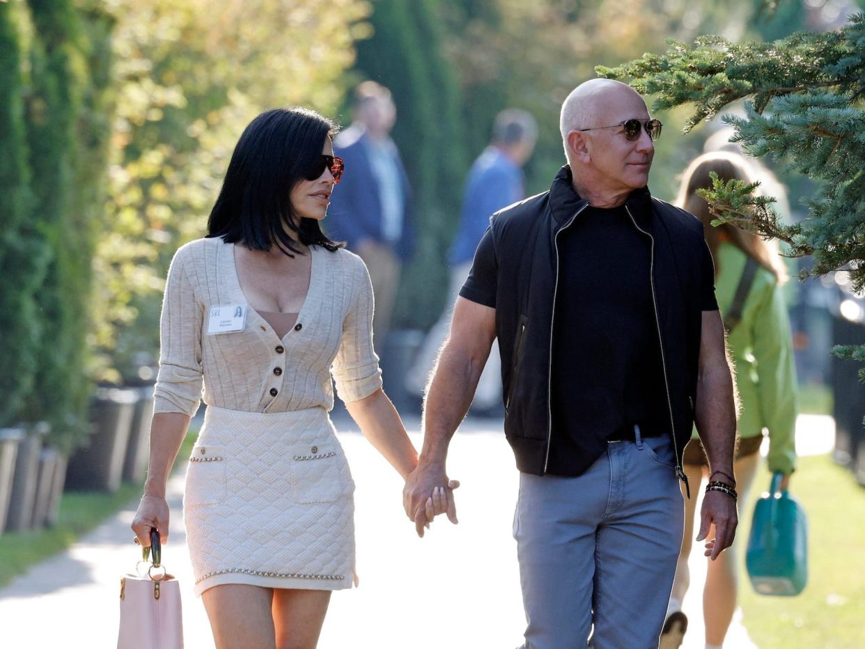 Lauren Sánchez and Jeff Bezos hold hands and walk on a sidewalk.