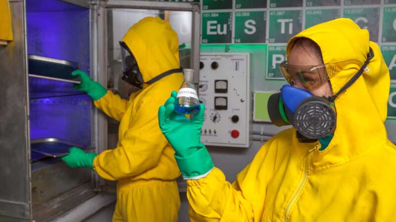 Two scientists in Hazmat suits cook methamphetamine in a laboratory.