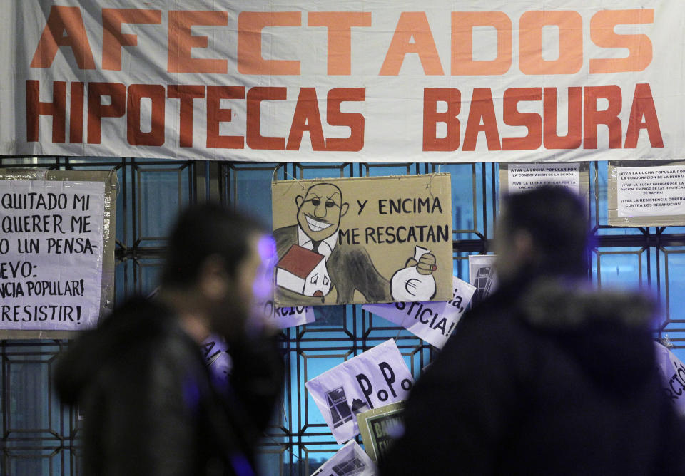 People walk by a banner reading "Rubbish mortgage" and a drawing of a banker reading "They even rescued me" during a protest against evictions outside Bankia's headquarter in Madrid, Saturday, Nov. 10, 2012. A woman in Spain jumped to her death as bailiffs approached to evict her Friday from her fourth-floor apartment for failing to pay the mortgage, officials said. It was the second apparent suicide linked to evictions, and it further illustrates the dire conditions many Spaniards find themselves in as the country's economy sinks. The government recently created a task force to study how to reduce evictions because of the devastating personal impact of repossessions due to tough Spanish mortgage rules and growing unease among the public on the subject. (AP Photo/Andres Kudacki)