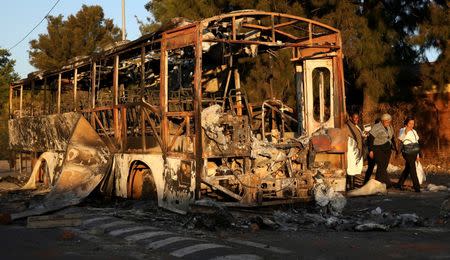 Locals walk past the remains of a burnt out bus used to barricade roads by protesters in Atteridgeville a township located to the west of Pretoria, South Africa June 21, 2016. REUTERS/Siphiwe Sibeko