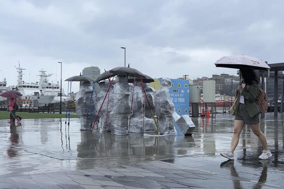 Residents with umbrellas walk past sculptures co covered up with plastic to protect from the incoming typhoon Khanun in the port city of Keelung near Taipei in northern Taiwan on Thursday, Aug. 3, 2023. (AP Photo/Johnson Lai)