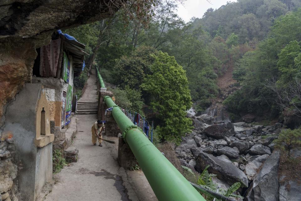 A woman sweeps outside her house next to a water pipeline from the Bagmati River in Sundarijaal, Nepal, on the outskirts of Kathmandu, Friday, April 22, 2022. (AP Photo/Niranjan Shrestha)