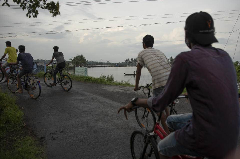 A fisherman rows his boat as youth pedal their bicycles in the morning in Kochi, Kerala state, India, Monday, June 1, 2020. More states opened up and crowds of commuters trickled onto the roads in many of India's cities on Monday as a three-phase plan to lift the nationwide coronavirus lockdown started despite an upward trend in new infections. (AP Photo/ R S Iyer)