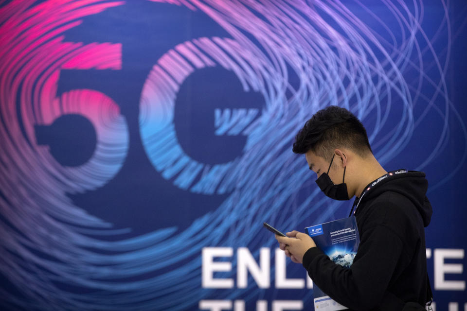 A man looks at his smartphone as he walks past a sign advertising 5G services at the PT Expo in Beijing, Wednesday, Sept. 14, 2020. China's leaders vowed Thursday, Oct. 29, 2020, to speed up its development as a self-reliant "technology power" amid a feud with Washington that is cutting access to U.S. components and hampering Beijing's industrial ambitions. (AP Photo/Mark Schiefelbein)