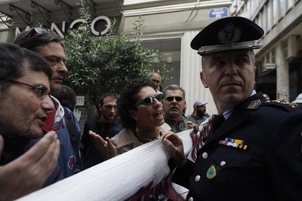 Protesters argue with a police officer during a protest against the opening of shops on Sundays and the extension of working hours, in Athens' Ermou shopping street, on Sunday, April 13 2014. Fitch ratings agency warned the successful bond issue didn't mean an end to Greece's financial problems. In a report Friday it said the issue showed the country's progress but doesn't mean it will be able to finance itself on its own when the bailout program ends later this year. (AP Photo/Kostas Tsironis)