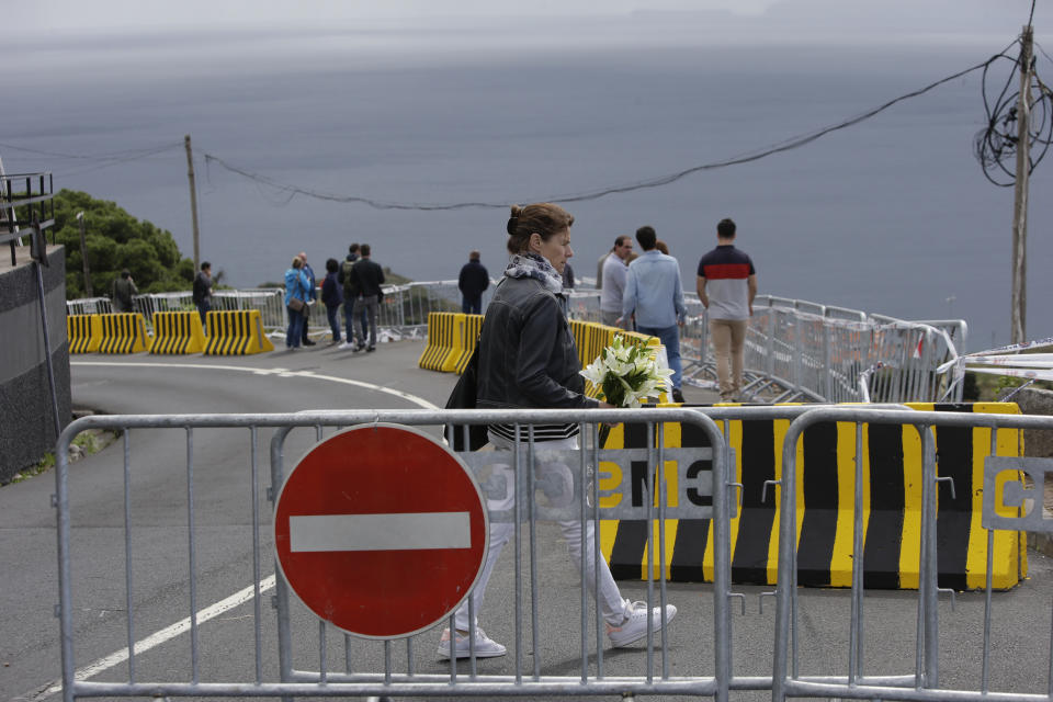 A woman walks to place flowers at the spot where a tourist bus veered off the road killing 29 people in Funchal, the capital of Portugal's Madeira Island, Friday April 19, 2019. A German plane is expected to arrive Friday in Madeira to take home survivors from the bus accident that killed 29 tourists after it veered off the road and plunged down a slope. All the deceased were German. The bus carried 55 people, including a Portuguese driver and guide. Sixteen people remain hospitalized, but authorities said all of them are out of danger. (AP Photo/Armando Franca)