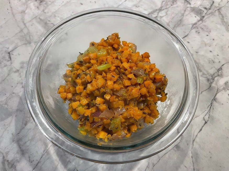 Clear glass bowl of orange cooked holiday hash on a gray counter