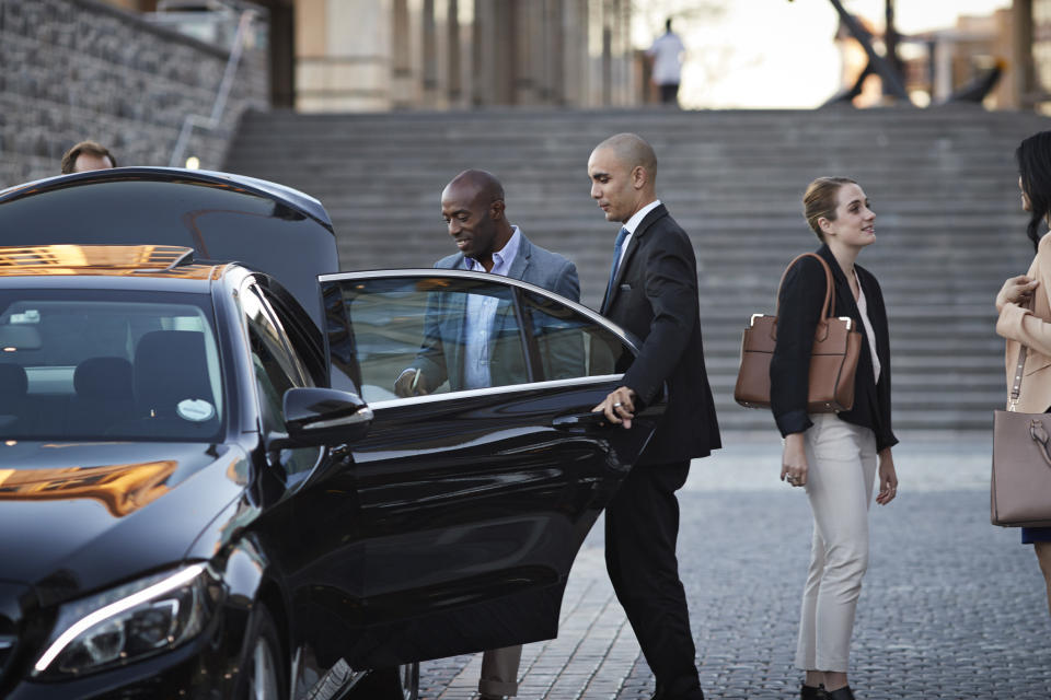 A man getting into a car held open by another man