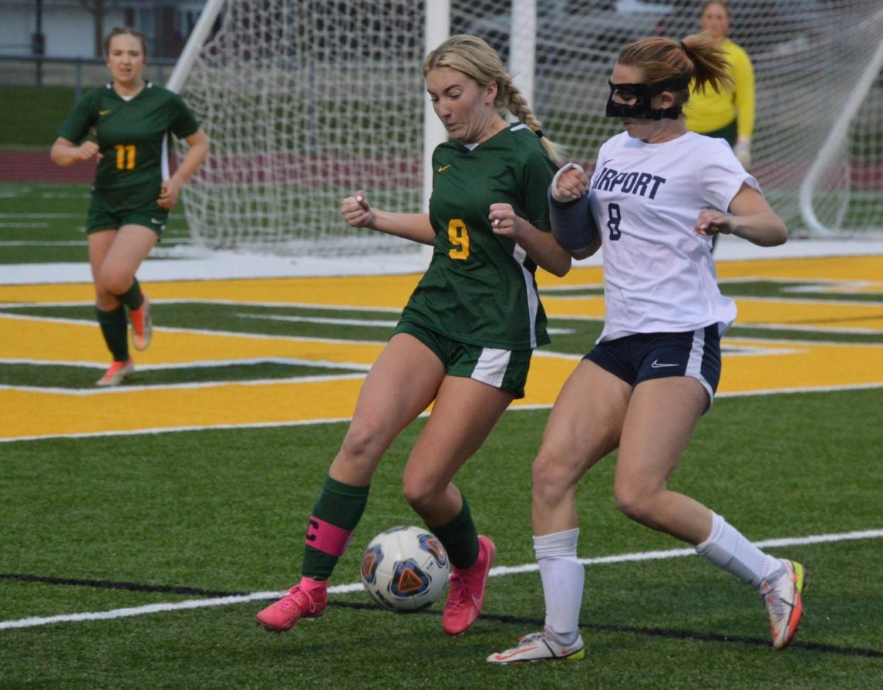 Airport’s Cecelia Ortega (right) and Megan Woelkers of Flat Rock for the ball in a recent game. Ortega was playing with a cast on her broken arm and a mask protecting her broken nose.