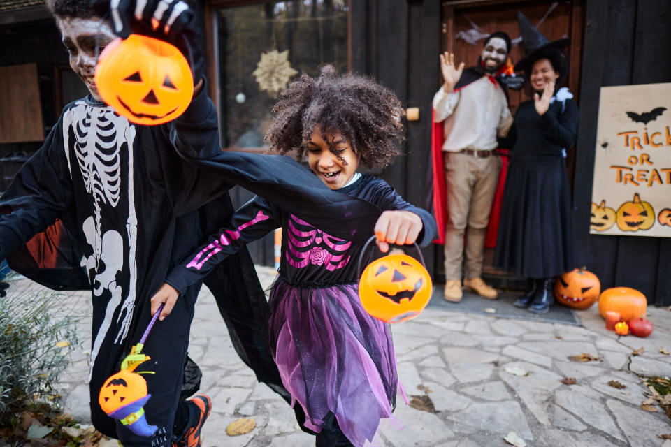 Children dressed in skeleton and witch costumes holding pumpkin buckets and trick-or-treating