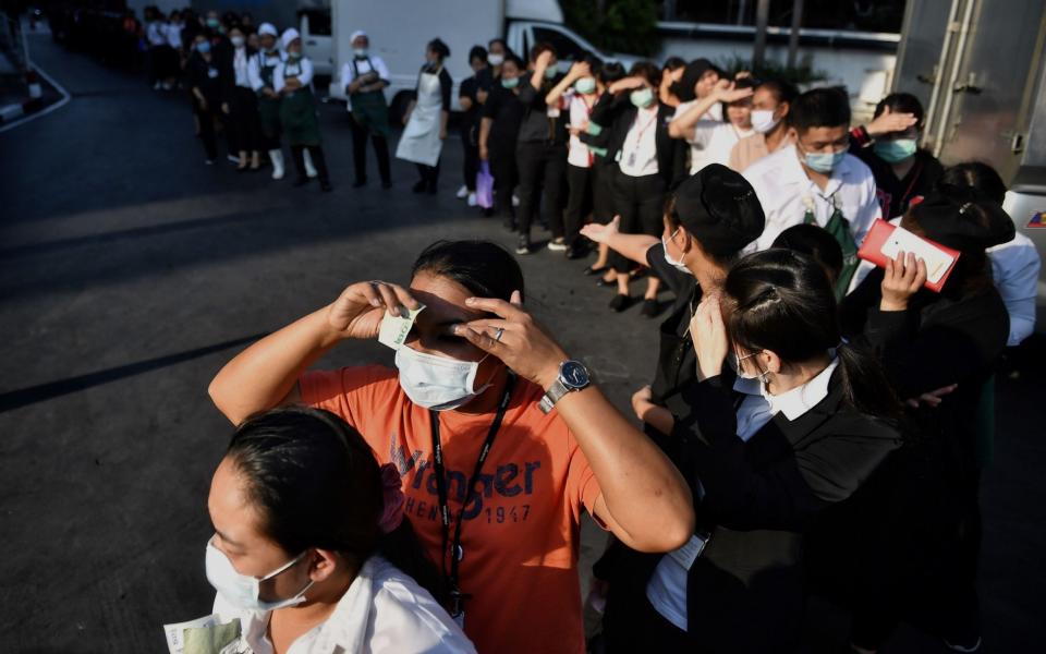 People line up to buy face masks and other discounted basic goods such as eggs and cooking oil during the launch of the government's mobile caravan by the Ministry of Commerce outside a shopping mall in Bangkok - LILLIAN SUWANRUMPHA / AFP