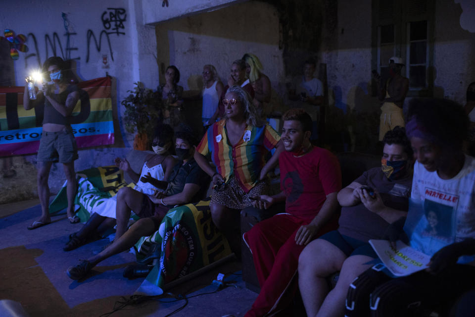 Indianara Siqueira, wearing a rainbow colored shirt, sits with fellow residents to watch their weekly presentations performed on a makeshift stage at the squat known as Casa Nem, occupied by members of the LGBTQ community who are in self-quarantine as a protective measure against the new coronavirus, in Rio de Janeiro, Brazil, Saturday, May 23, 2020. Siqueira, 49, a transgender sex worker and activist leads Casa Nem. (AP Photo/Silvia Izquierdo)