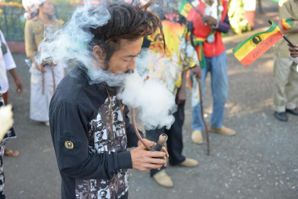 FILE - In this Feb. 6, 2013 photo, a Rastafarian named Bongho Jatusy smokes a pipe of marijuana outside a museum dedicated to the memory of late reggae icon Bob Marley in Kingston, Jamaica. While marijuana is still illegal in Jamaica, where it is known popularly as “ganja,” increasingly vocal advocates say that Jamaica could give its struggling economy a boost by taking advantage of the fact the island is nearly as famous for its marijuana as it is for beaches, reggae music and world-beating sprinters. Anxiety over U.S. reprisals has always doused reform efforts in Jamaica, including a broadly supported 2001 attempt to approve private use of marijuana by adults. (AP Photo/David McFadden, File)